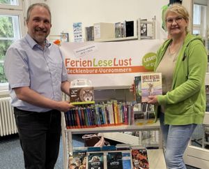 Maren Gläser vom Wildpark MV und Dr. Tilmann Wesolowski von der Bibliothek vor dem Regal des Ferienleseclubs FLL